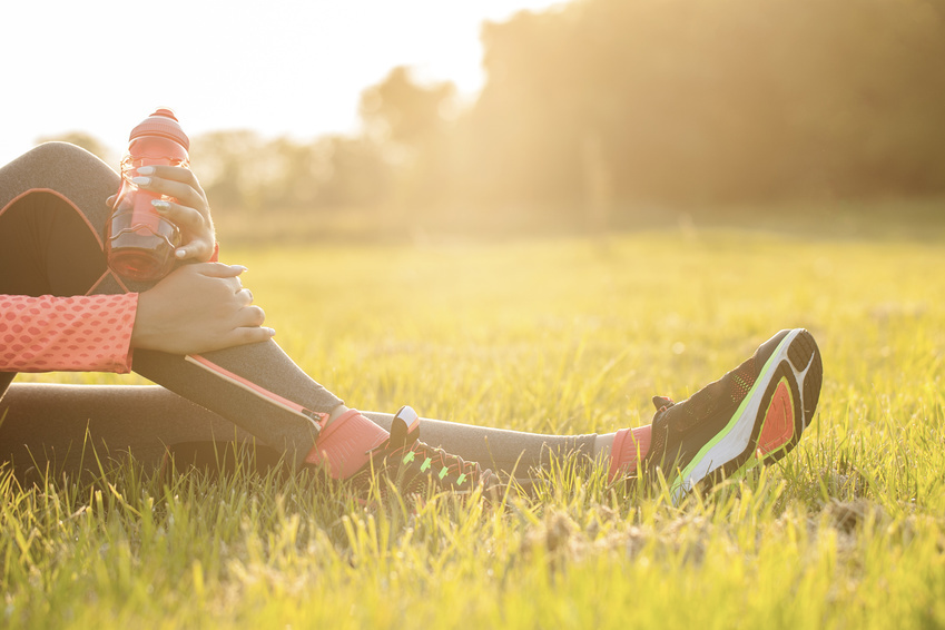 Eine Sportlerin sitzt in der Sonne auf der Wiese mit einer Trinkflasche in der Hand