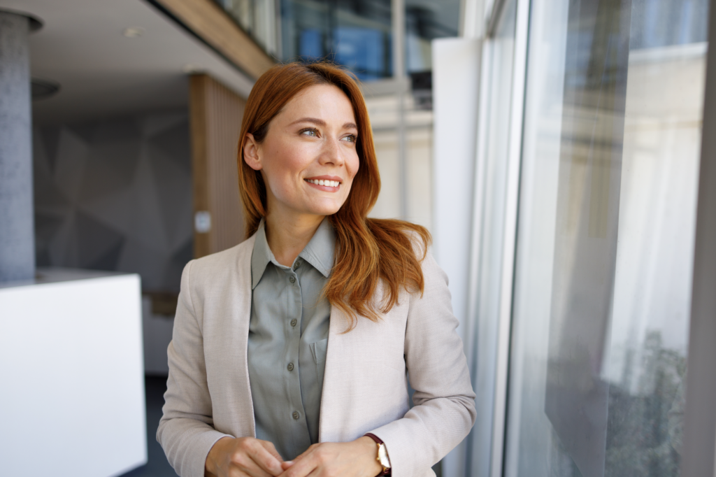 Businessfrau schaut entspannt und klar aus dem Fenster mit einem leichten Lächeln